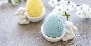Colorful Easter Eggs in stand with ceramic easter bunny figurines and spring blossom on grey concrete background